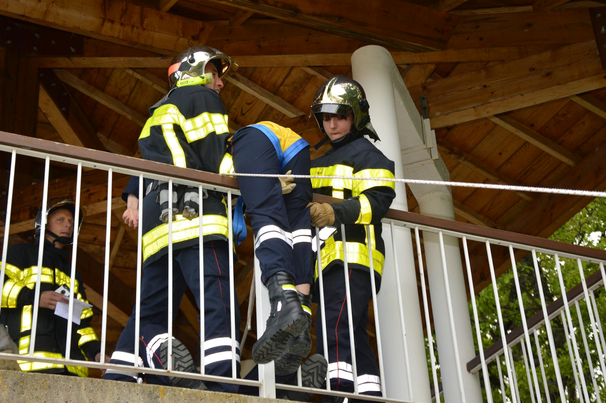 Firefighters practicing a rescue drill, holding a dummy over a railing, showcasing teamwork and safety.